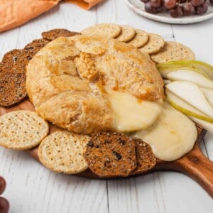 Baked brie in puff pastry on a wooden board with crackers and fruit.