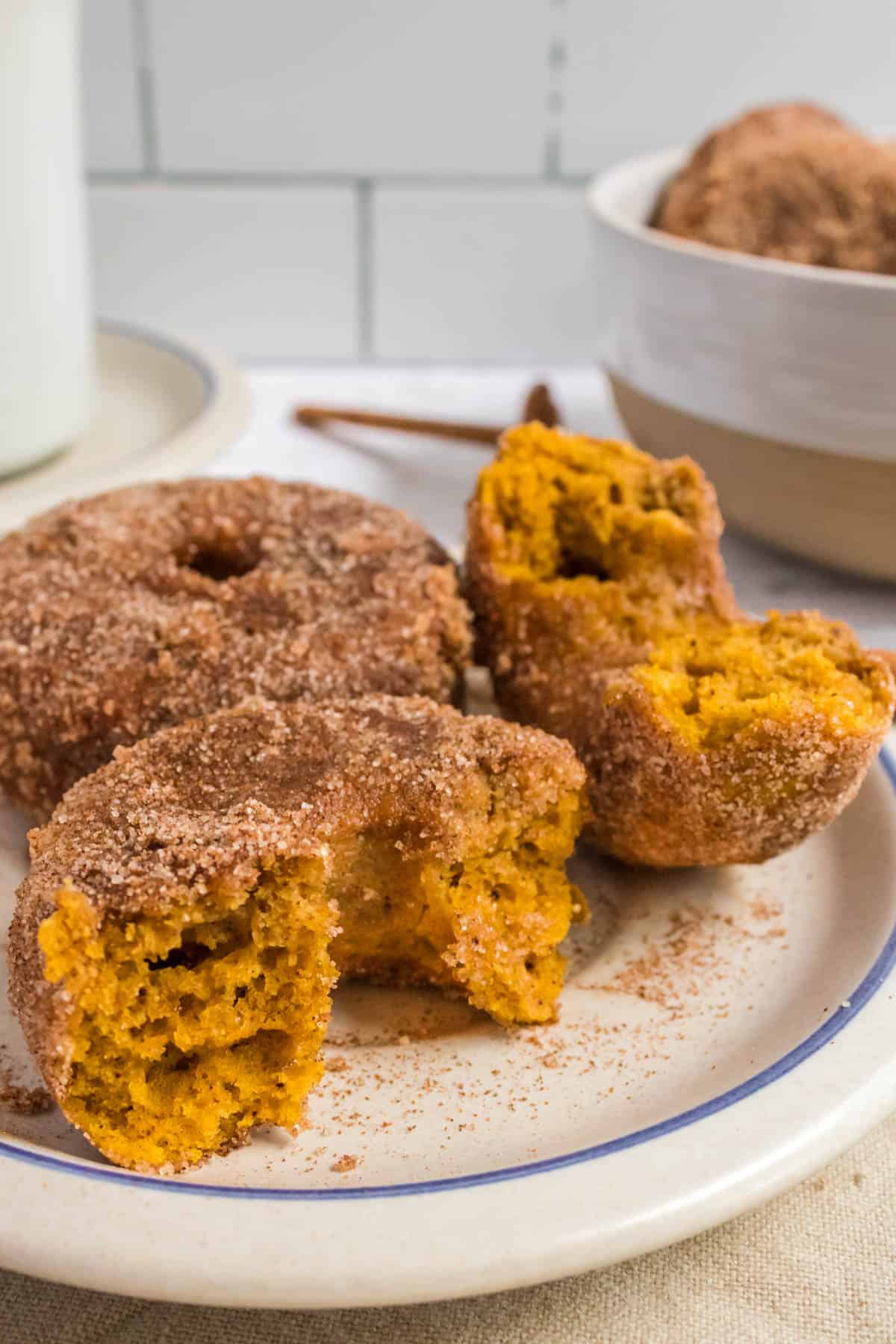 Baked pumpkin donuts covered in cinnamon sugar on a plate.