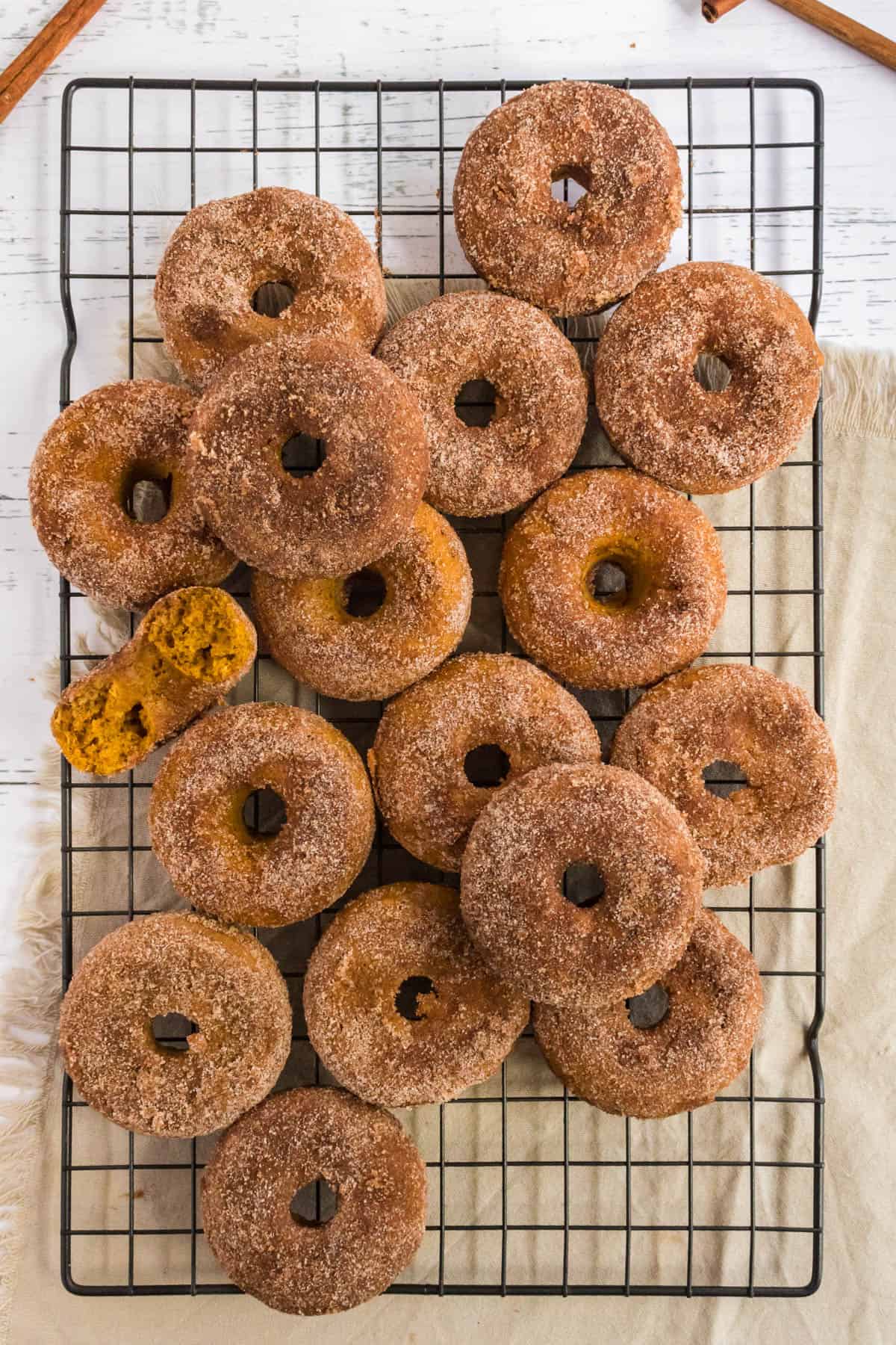 More than a dozen baked pumpkin donuts on a wire rack.