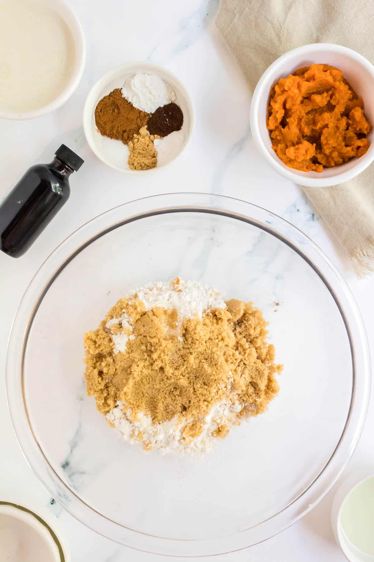 Brown sugar in a mixing bowl with pumpkin puree and spices around it.
