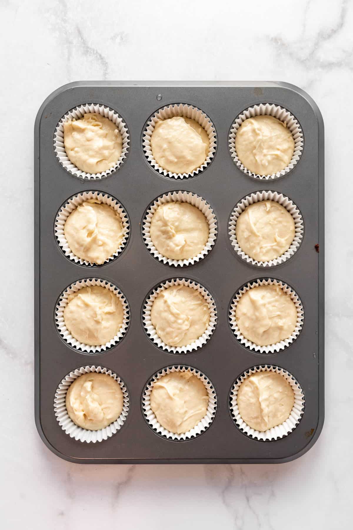 Coconut cupcake batter in paper liners in a muffin pan.