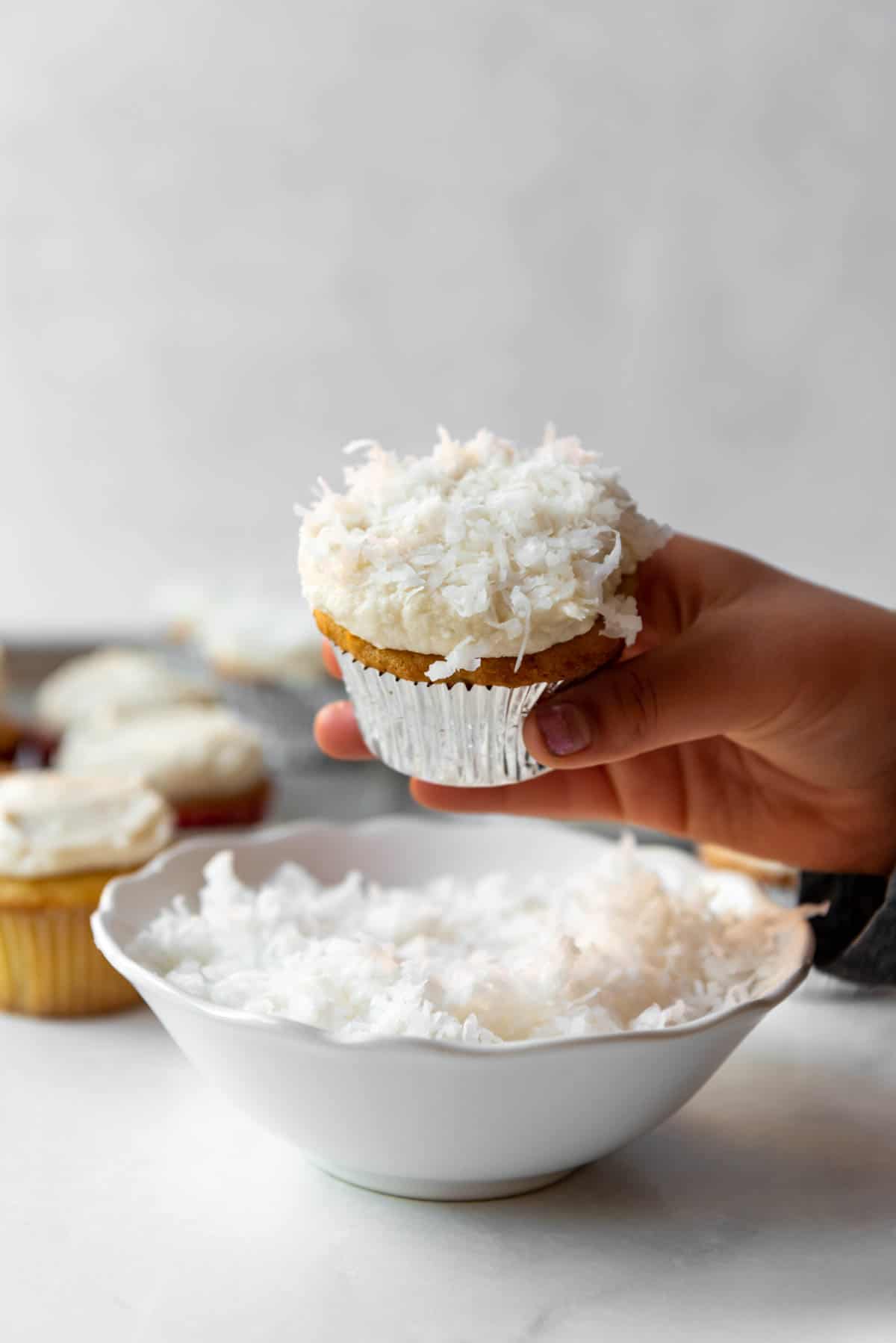 A hand holding a coconut cupcake.