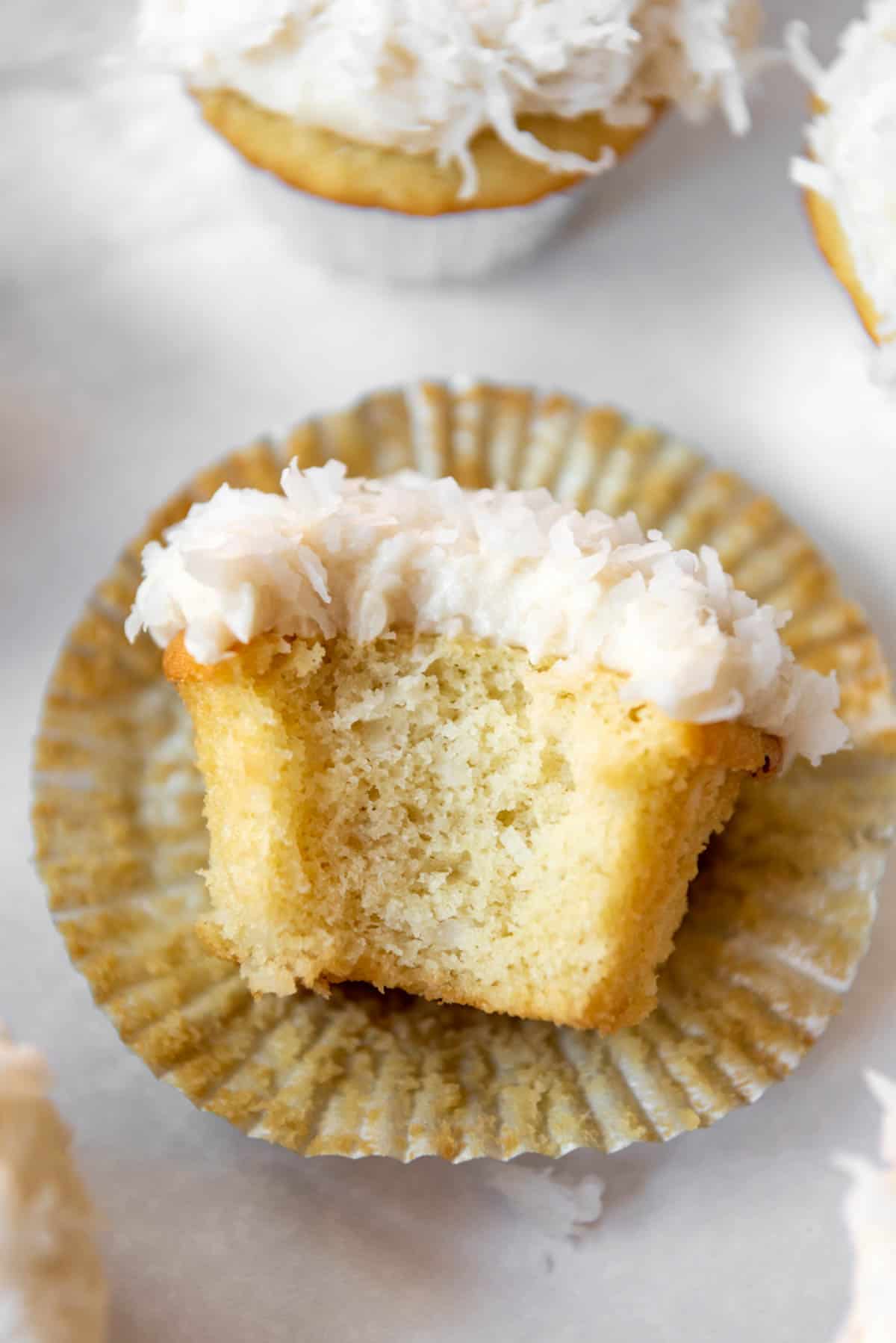An unwrapped coconut cupcake on it's wrapper with a bite taken out of it.
