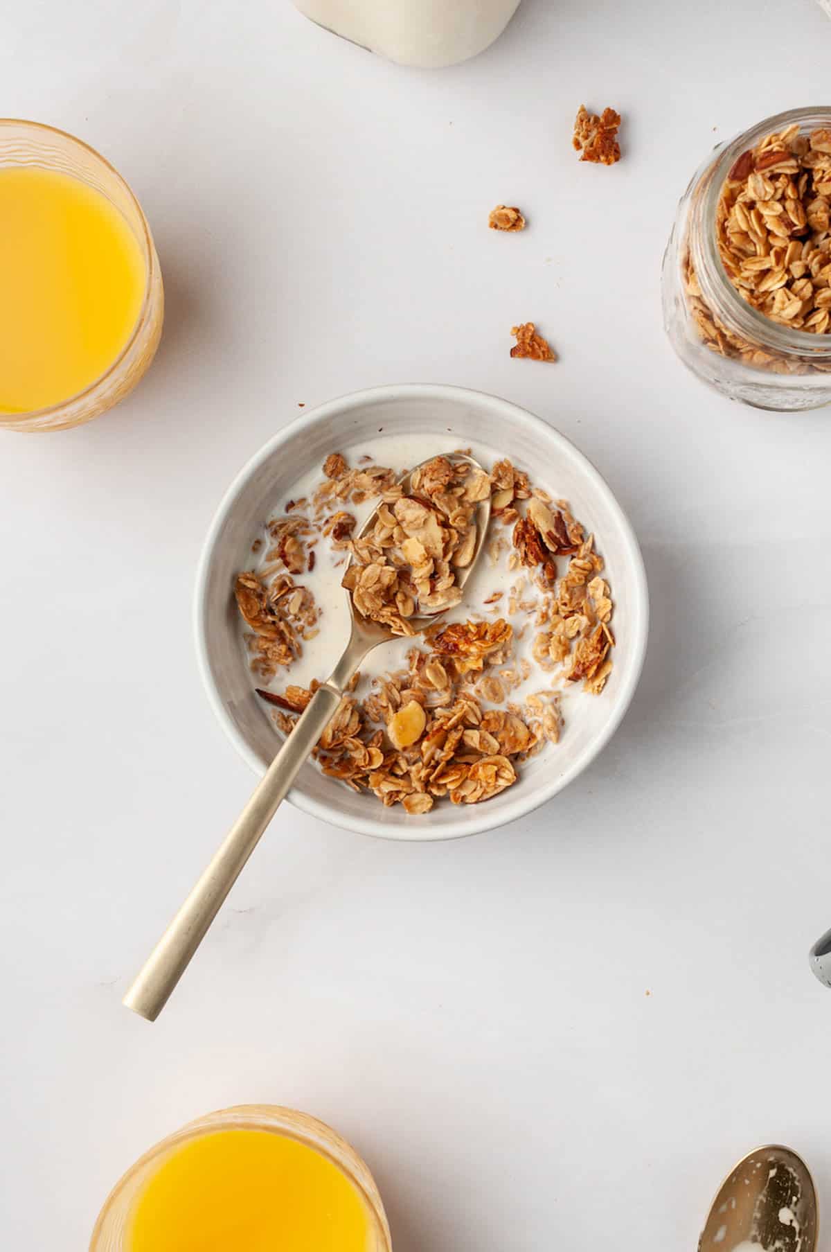 A bowl of granola cereal with milk next to glasses of orange juice.