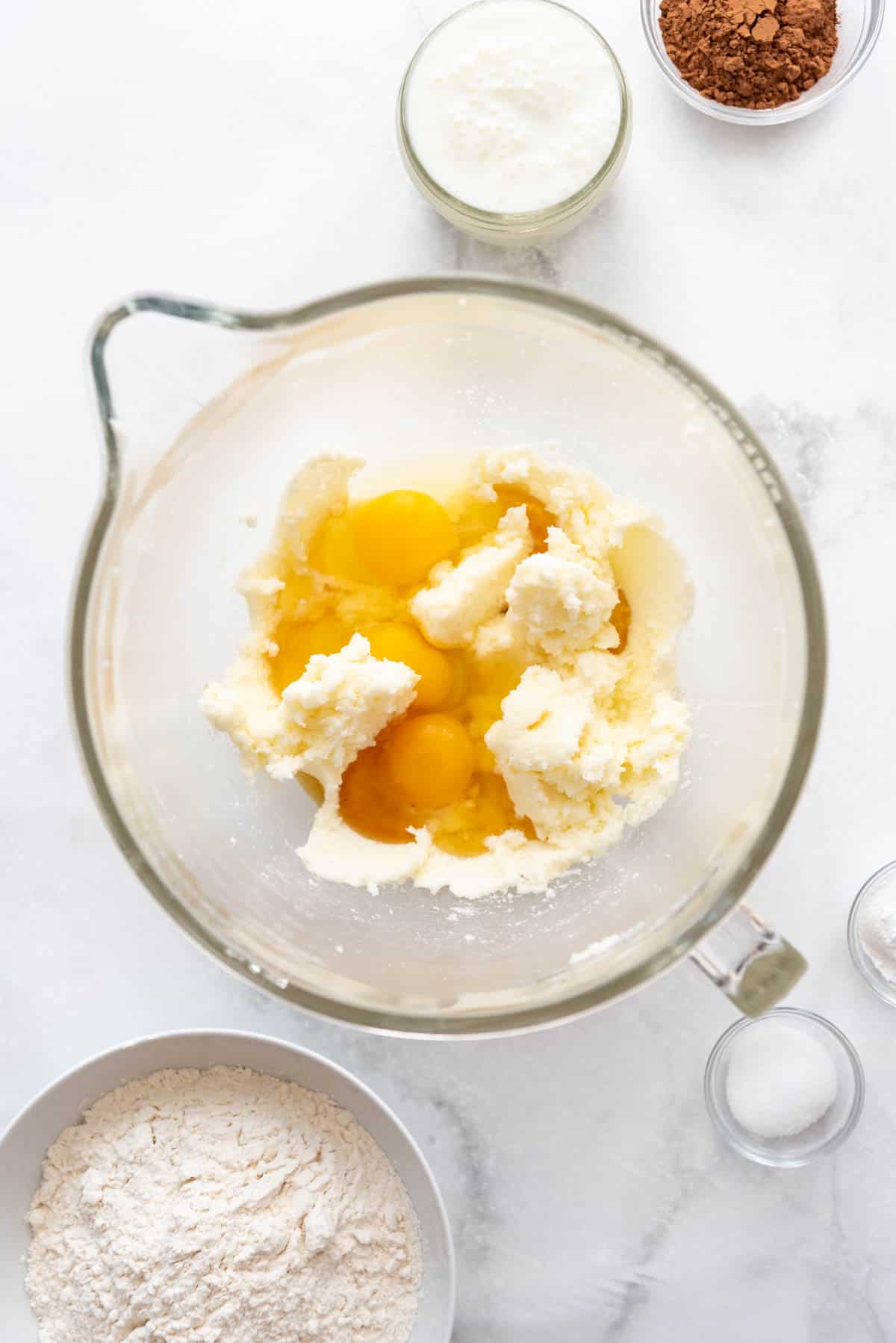 Adding eggs and vanilla extract to creamed butter and sugar in a large glass mixing bowl.