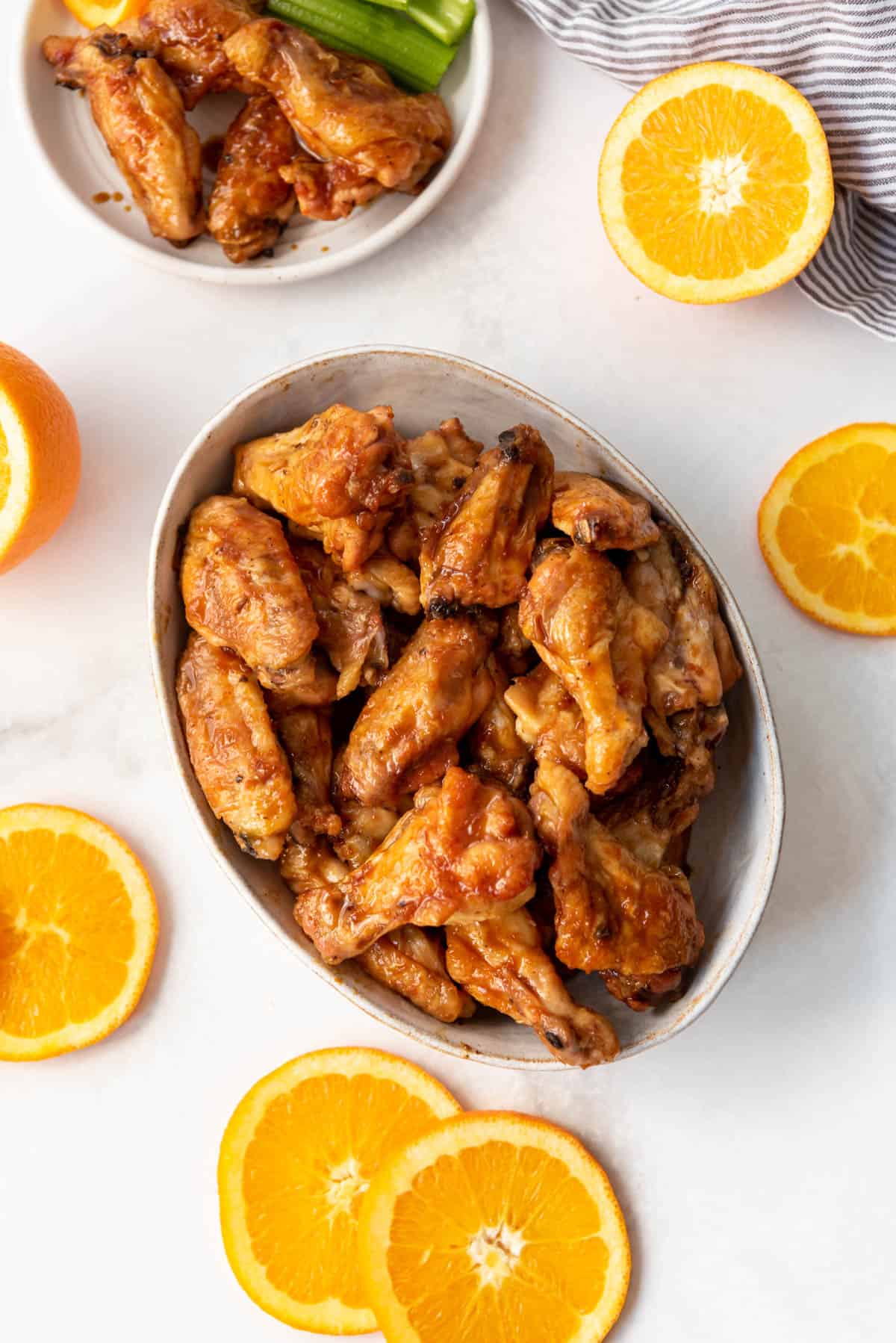 An overhead image of a serving bowl of orange glazed chicken wings surrounded by orange slices.