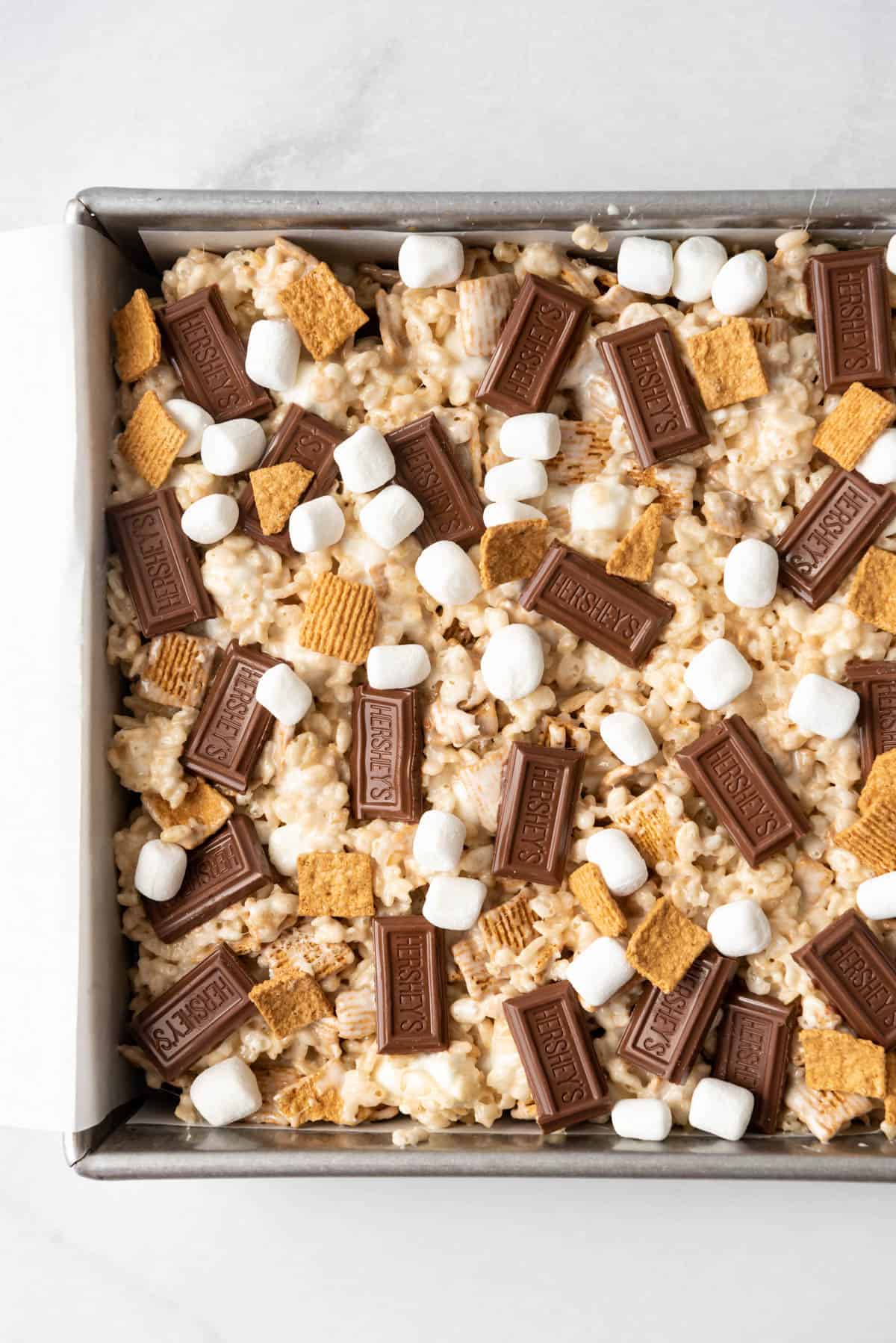 A close image of s'mores rice krispie treats with golden grahams cereal, marshmallows and chocolate bars sprinkled on top.