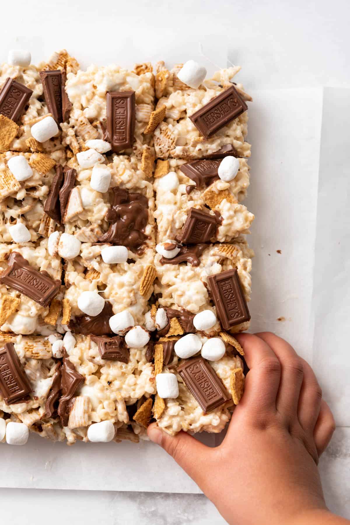 A child's hand pulling a s'mores rice krispie treat away from more cereal squares.
