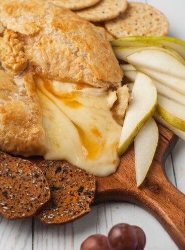 Baked brie oozing onto board with crackers and pears