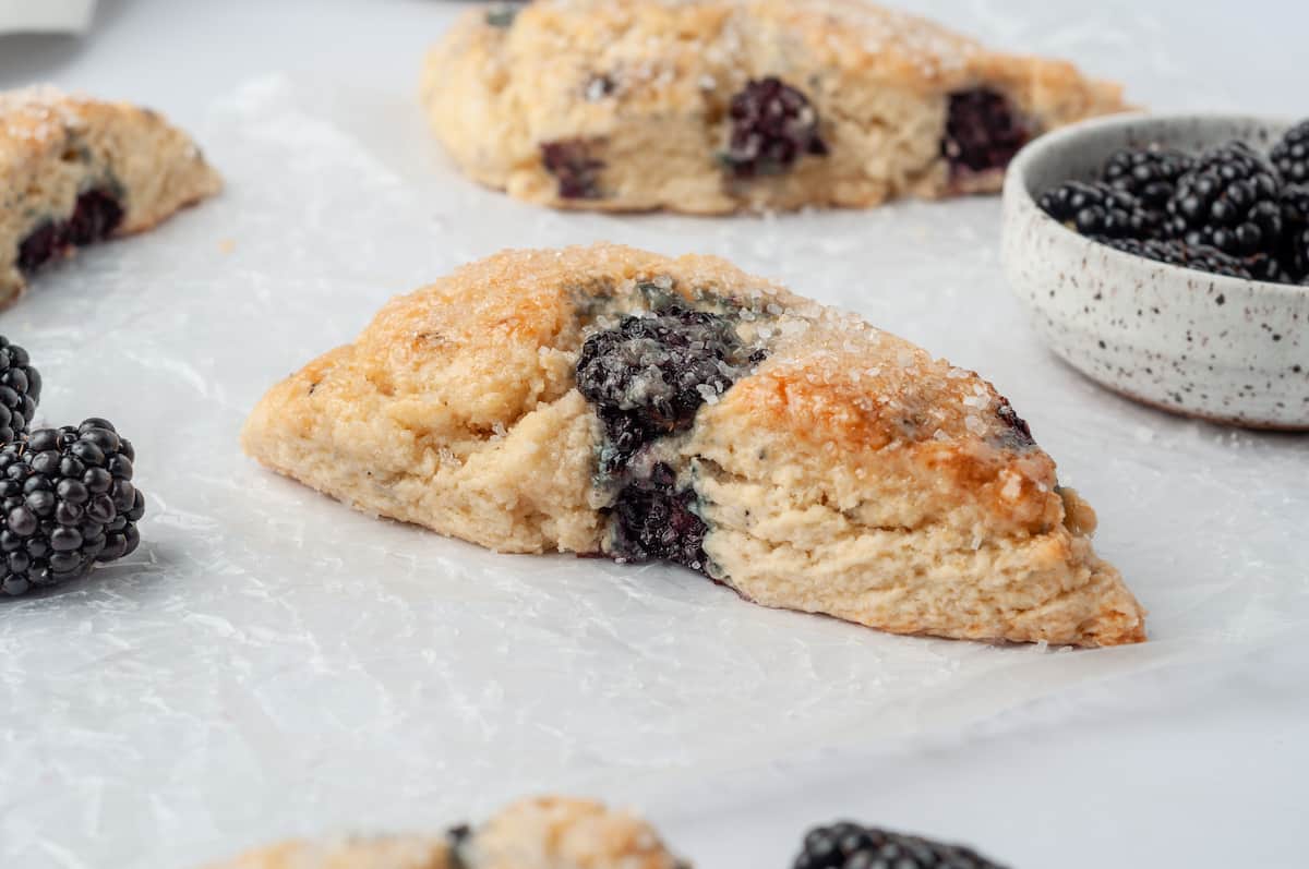 Blackberry scones on parchment paper with bowl of berries