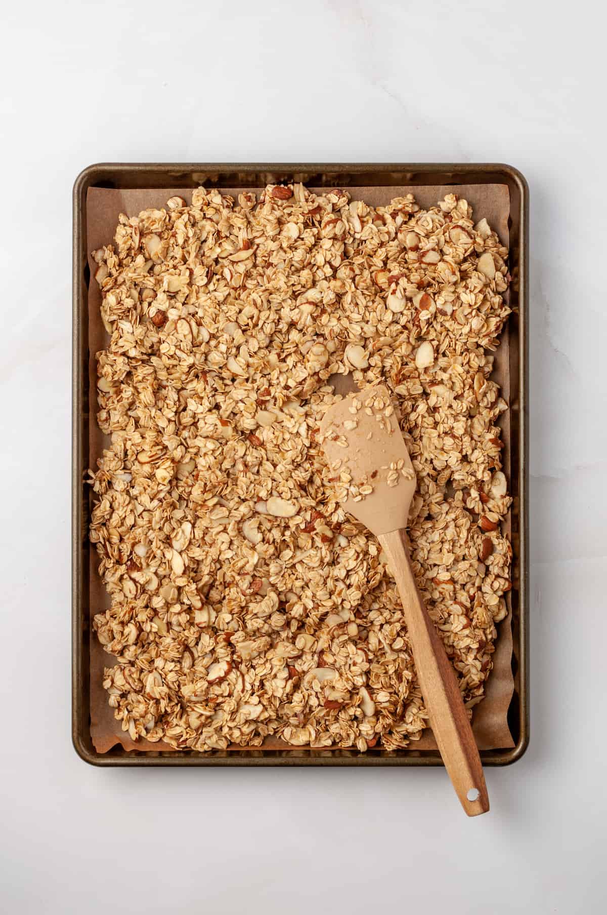 Overhead view of granola on sheet pan with wooden spatula
