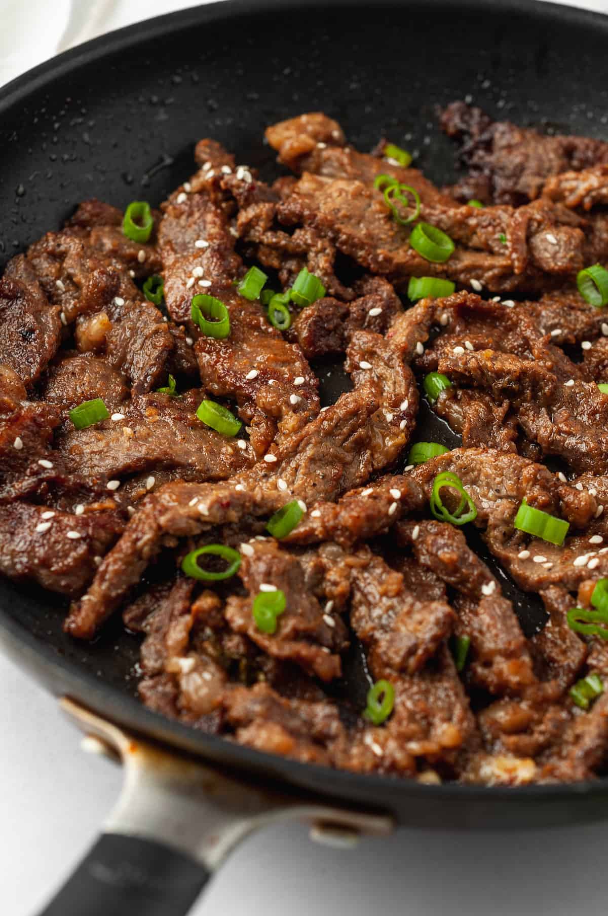 Bulgogi in skillet with sliced green onions and sesame seeds