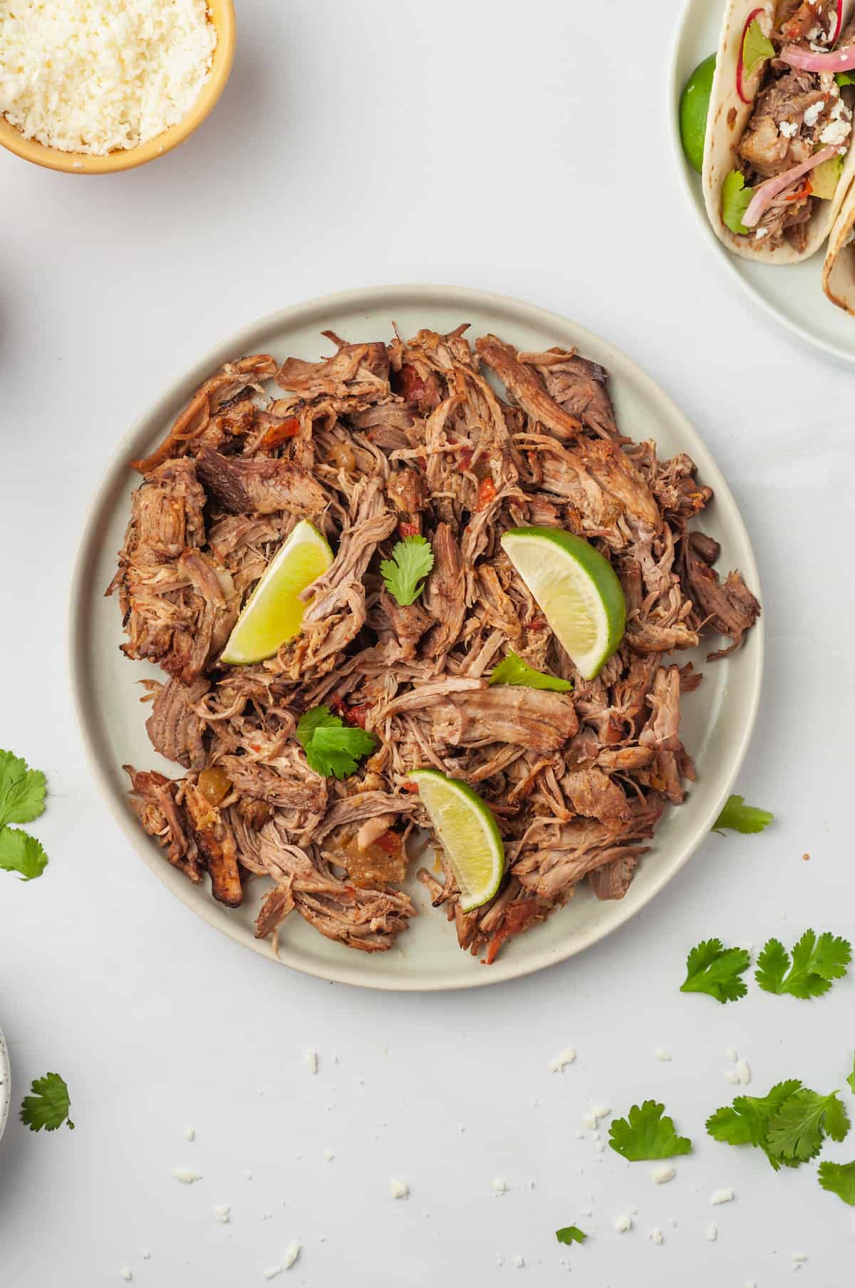 Plate of pork carnitas garnished with lime wedges and cilantro