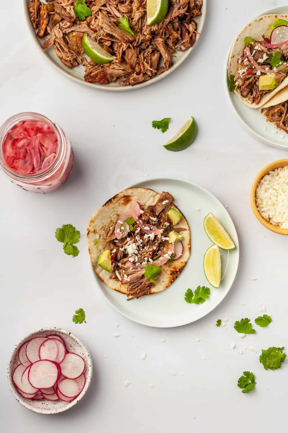 Pork carnitas taco on plate surrounded by bowls of toppings