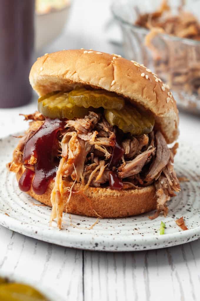 Pulled pork sandwich on plate topped with barbecue sauce and pickles