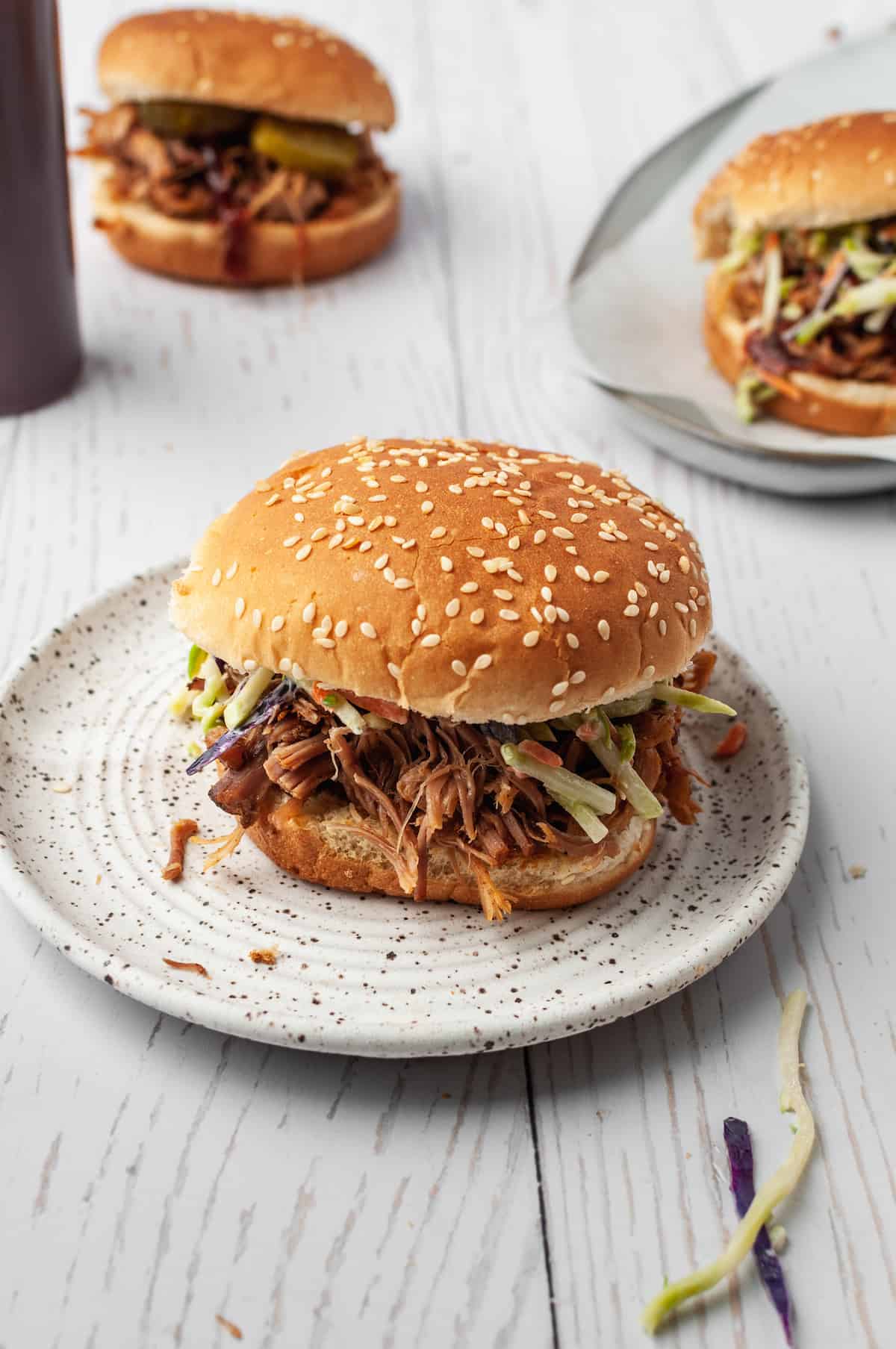 Pulled pork sandwich on plate with 2 sandwiches in background