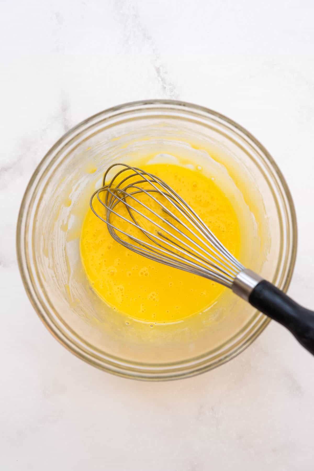 Whisking egg yolks and sugar together in a glass mixing bowl.