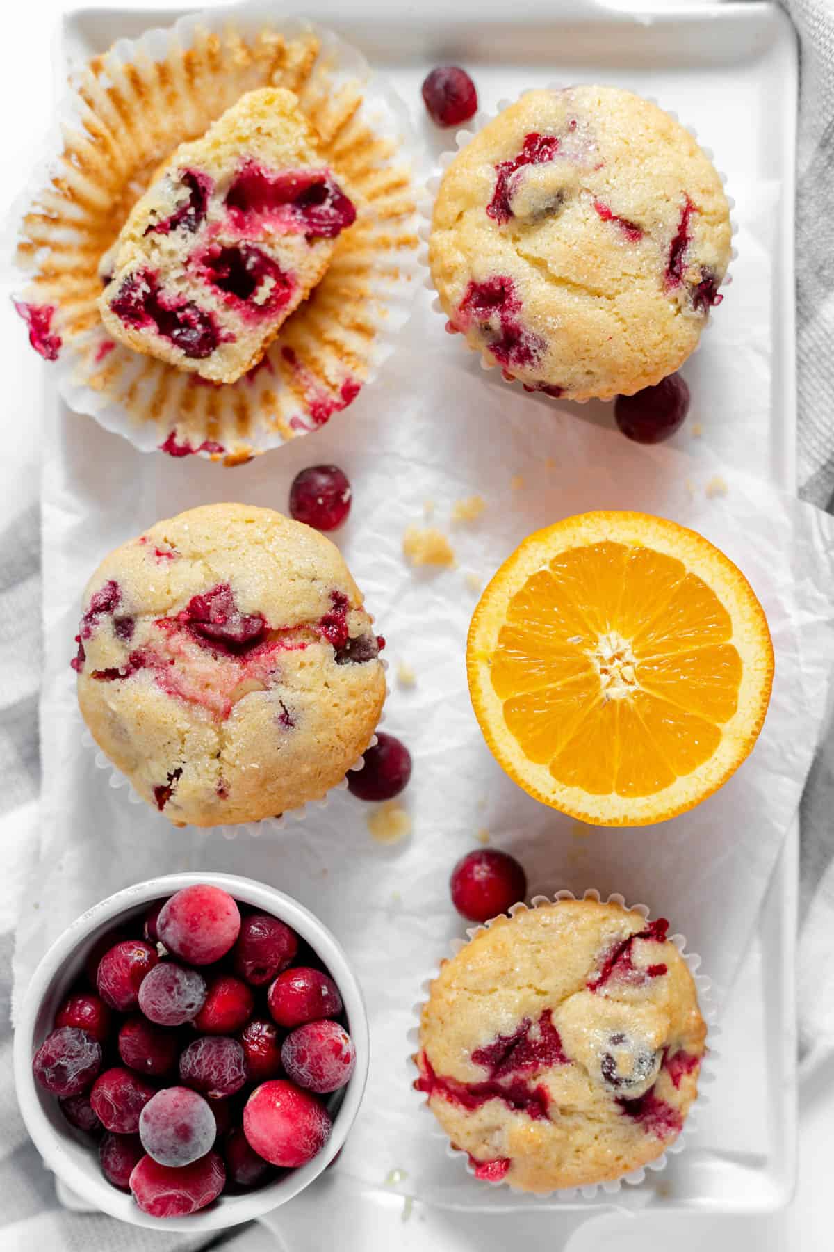 Cranberry orange muffins next to a bowl of cranberries and half an orange.