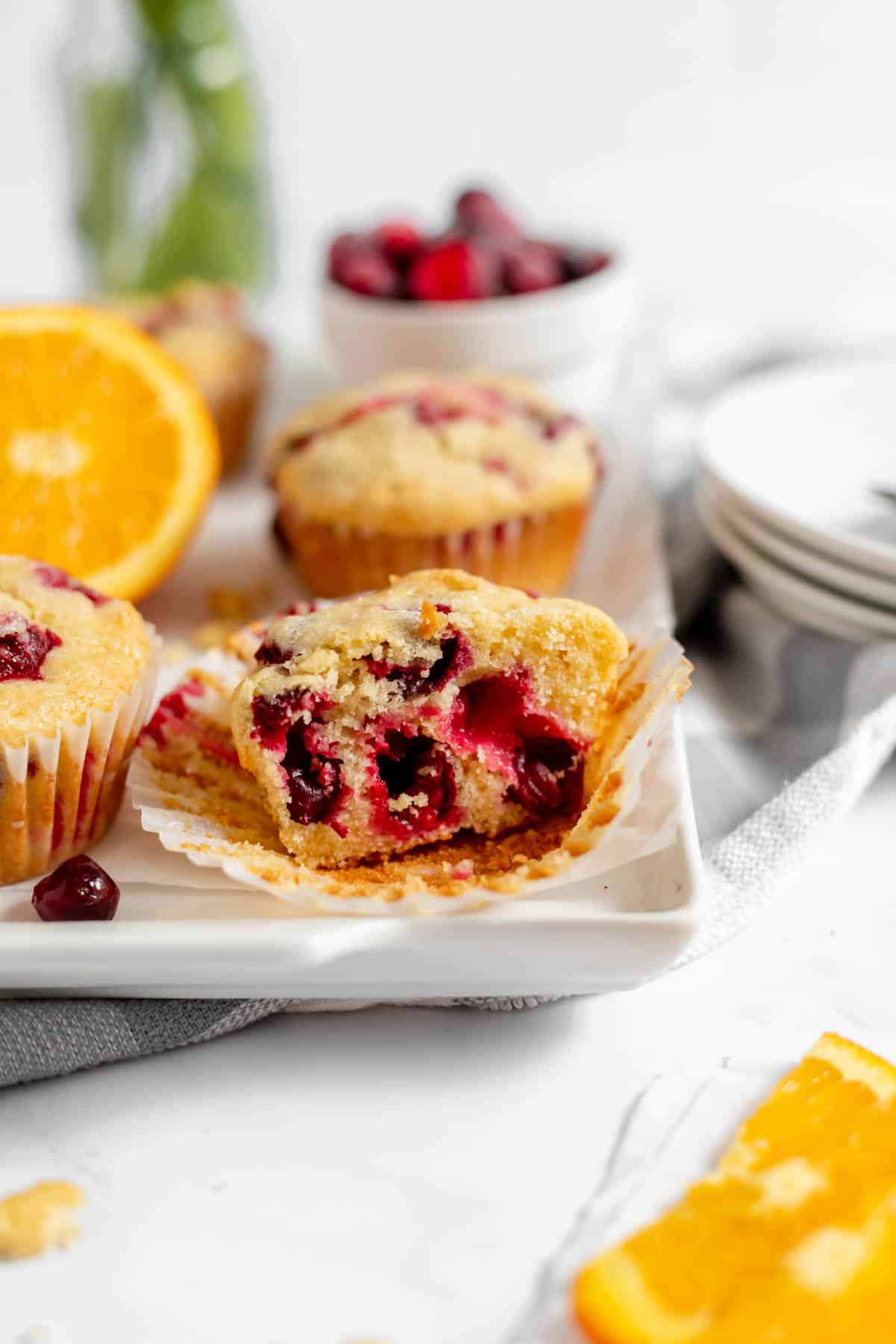 An unwrapped half of a cranberry orange muffin on a white plate.