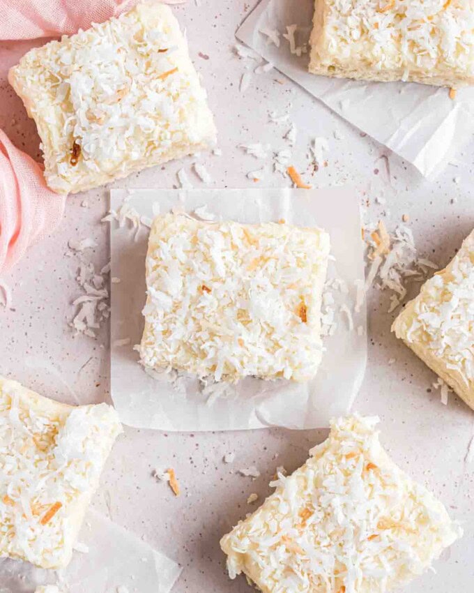 Frosted coconut sugar cookie bars with sweetened shredded coconut sprinkled on top and around them.