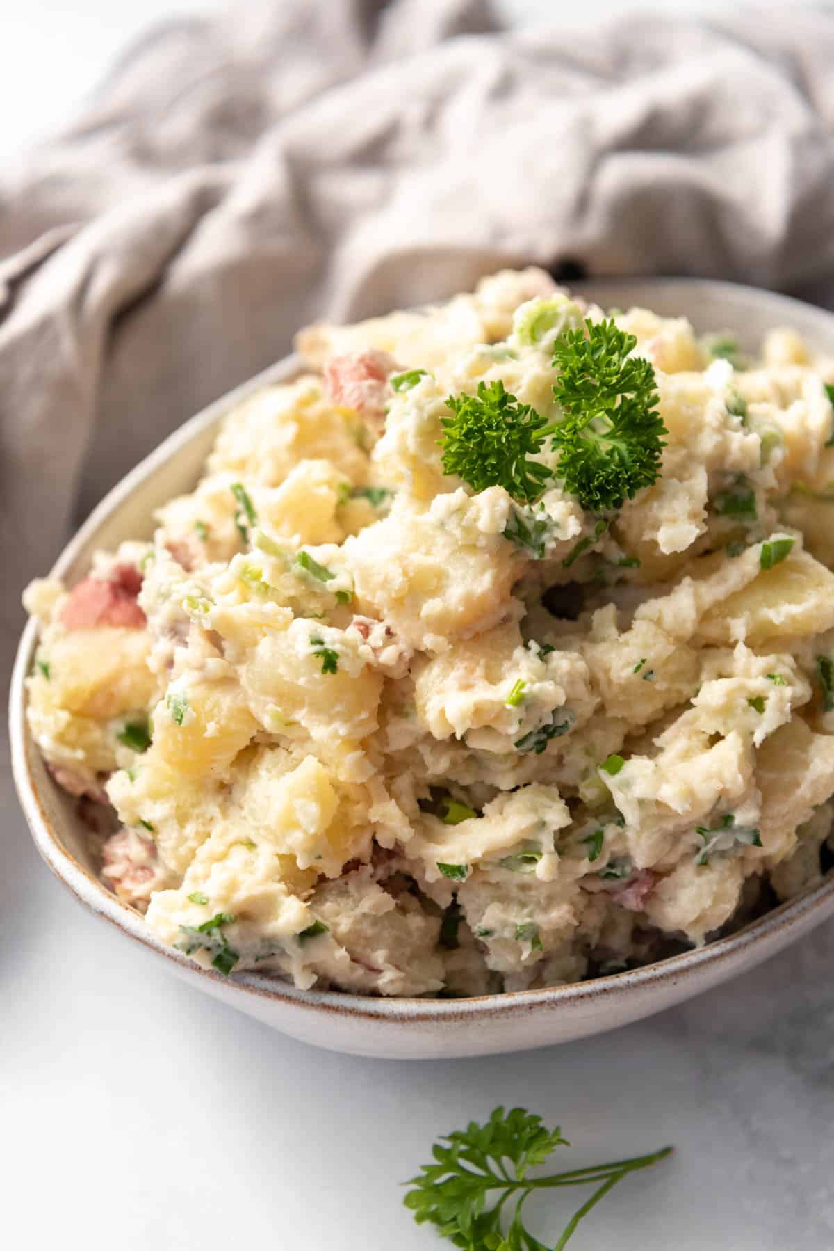 A serving bowl filled with Greek potato salad with sprigs of fresh parsley.