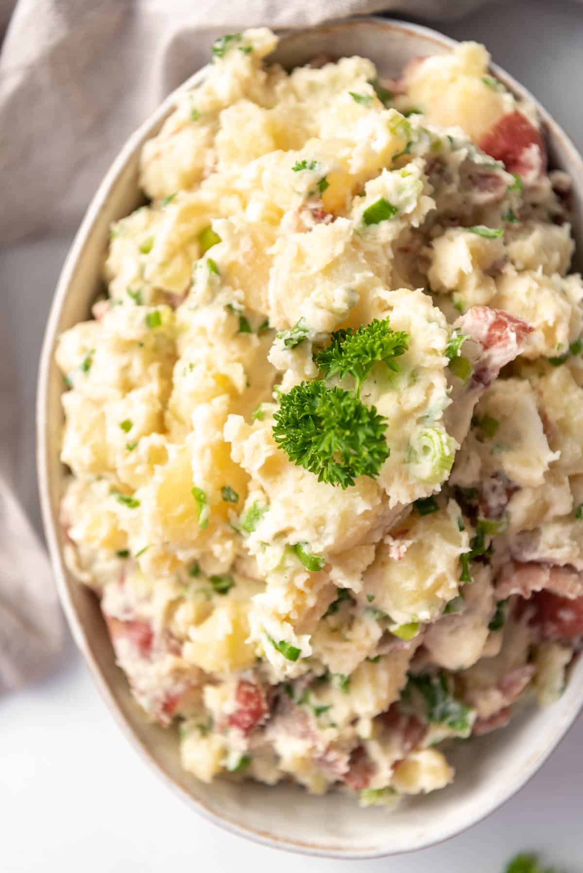 A sprig of parsley on top of a bowl of Greek potato salad.