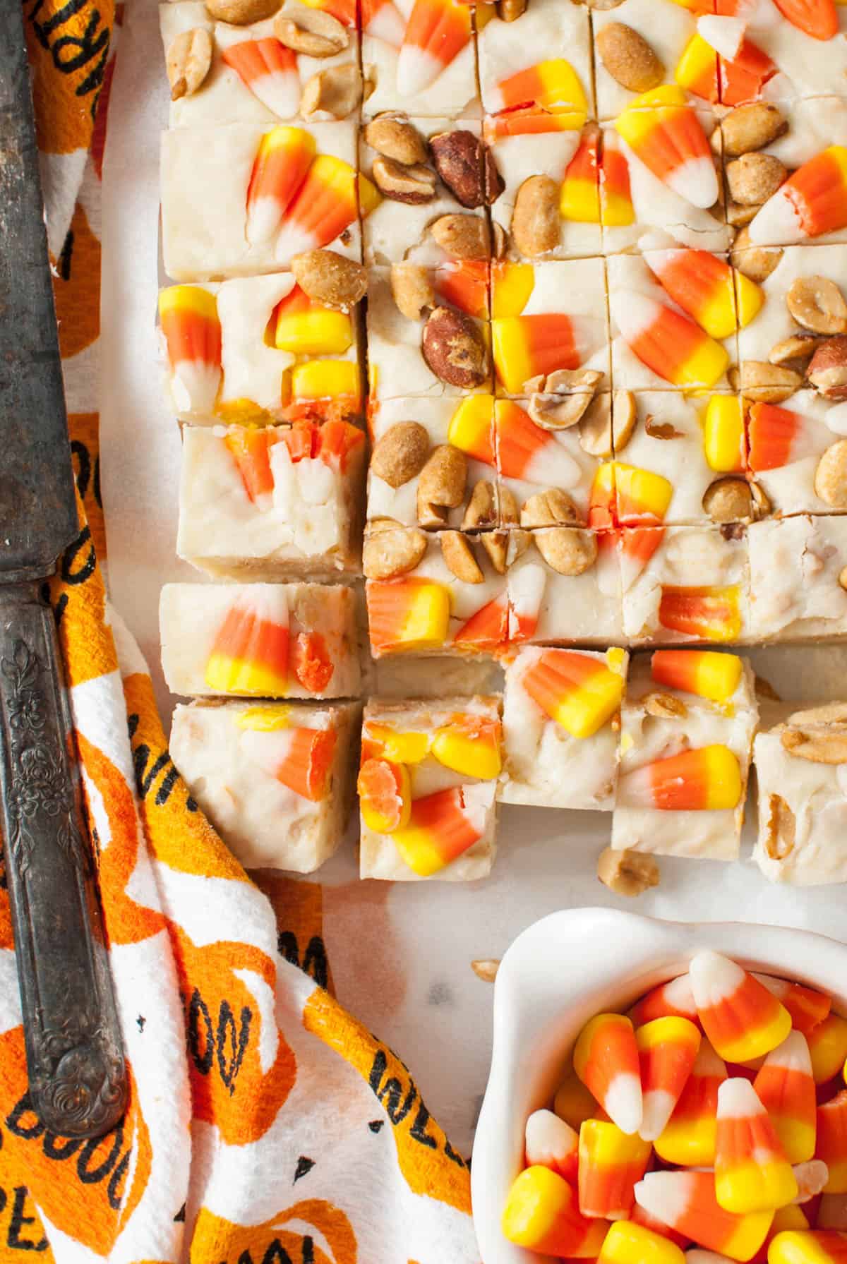 Small squares of Halloween candy corn fudge with peanuts in rows next to a bowl of candy corn.