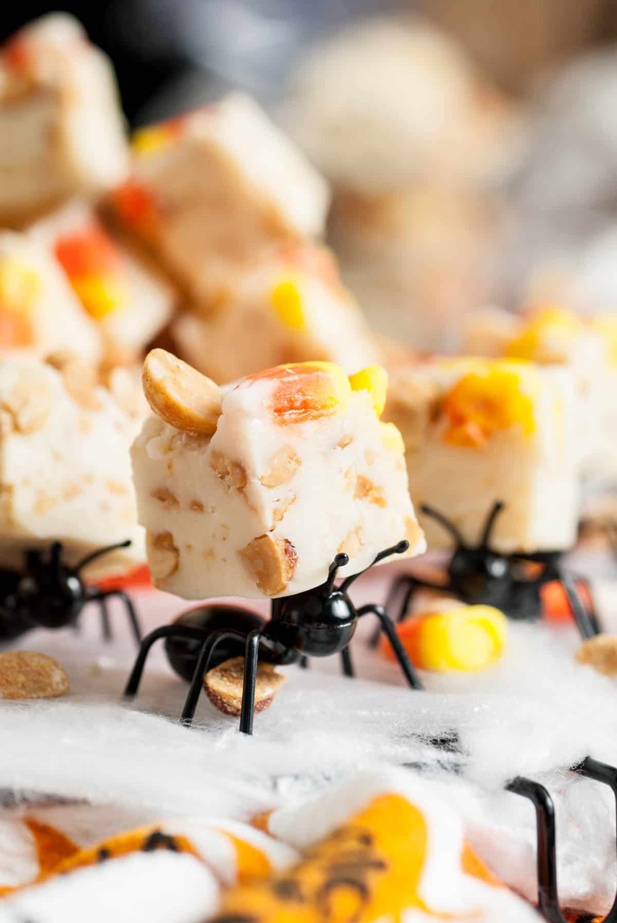 A plastic ant carrying a piece of candy corn fudge on its back.