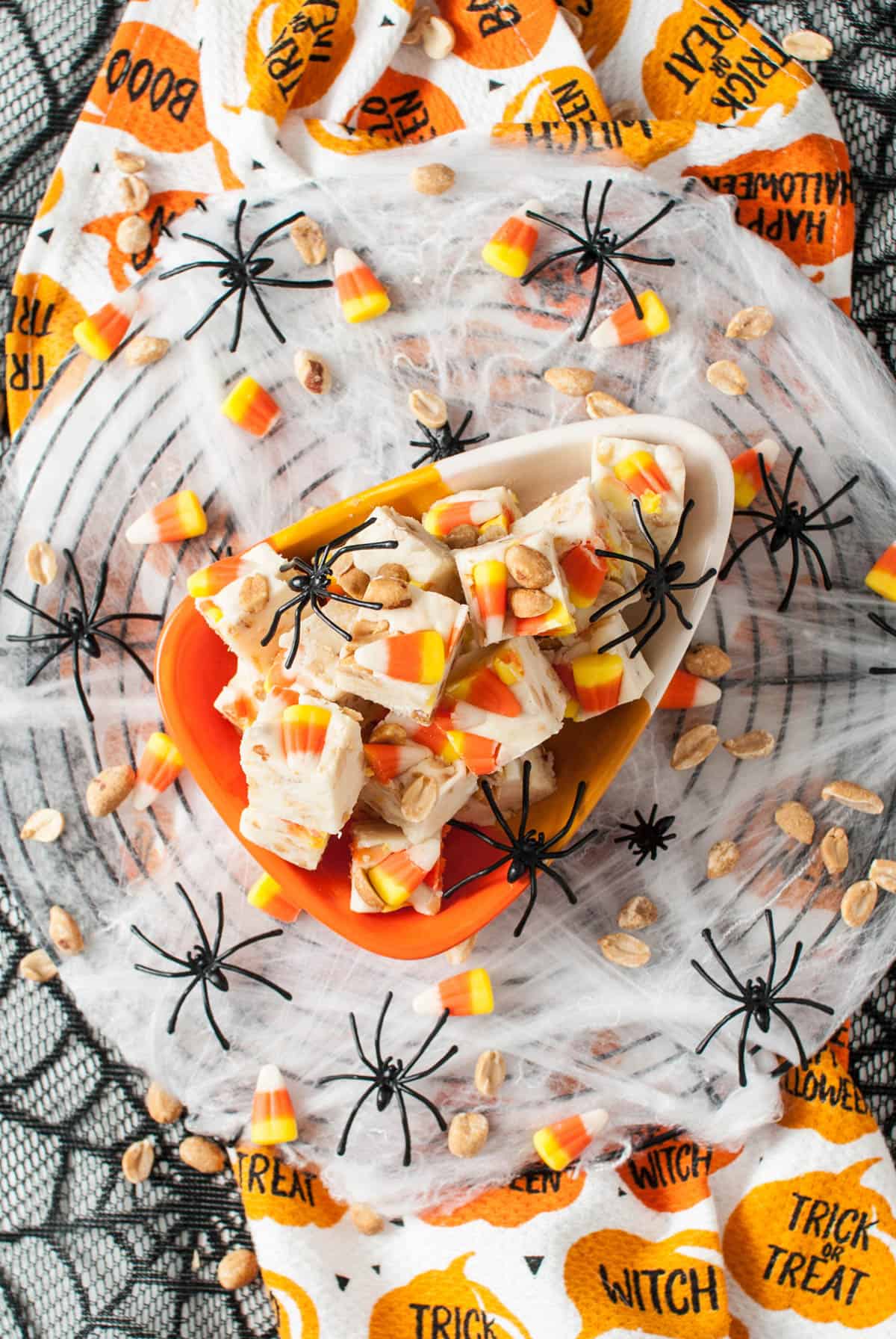 A Halloween plate filled with squares of candy corn fudge with black plastic spiders around it.