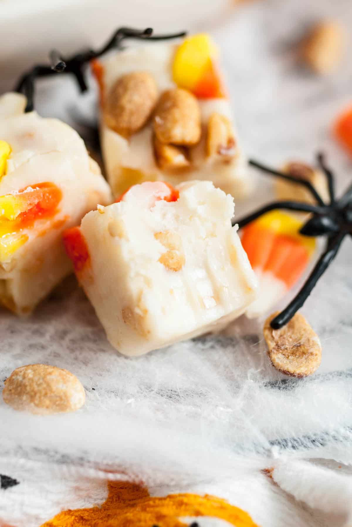 A piece of candy corn peanut white chocolate fudge with a bite taken out of it.