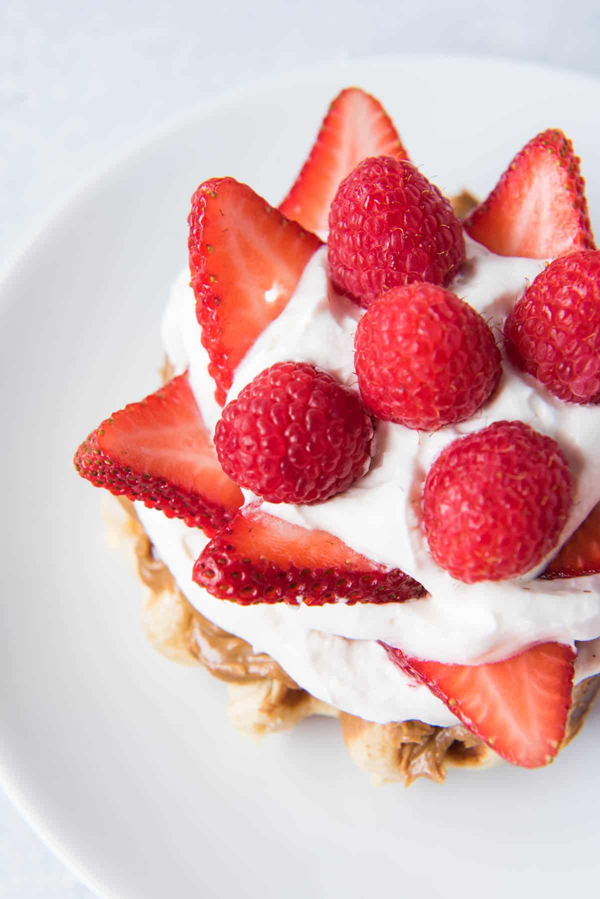 A cream and berry topped waffle on a white plate.