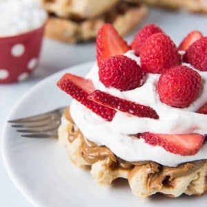 Stacks of waffles in the background with a waffle in front covered in spreads and fresh berries.