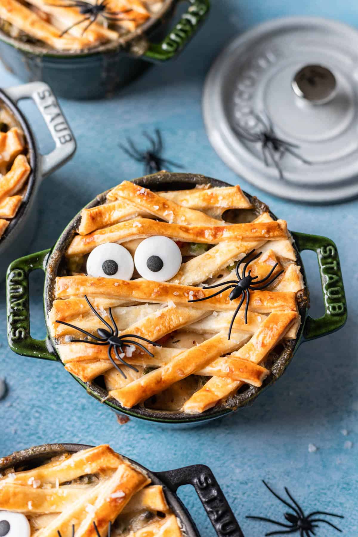 A mummy pot pie decorated with strips of pie crust, eyeball sprinkles, and plastic spiders.