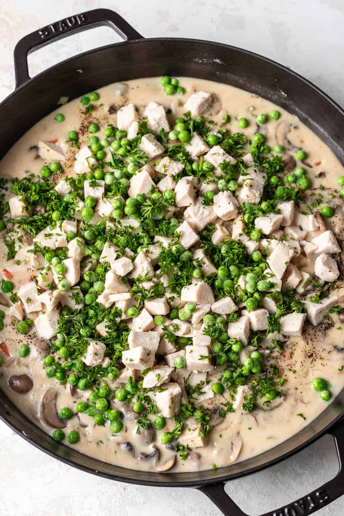 Adding cooked, cubed chicken and peas to chicken pot pie filling.