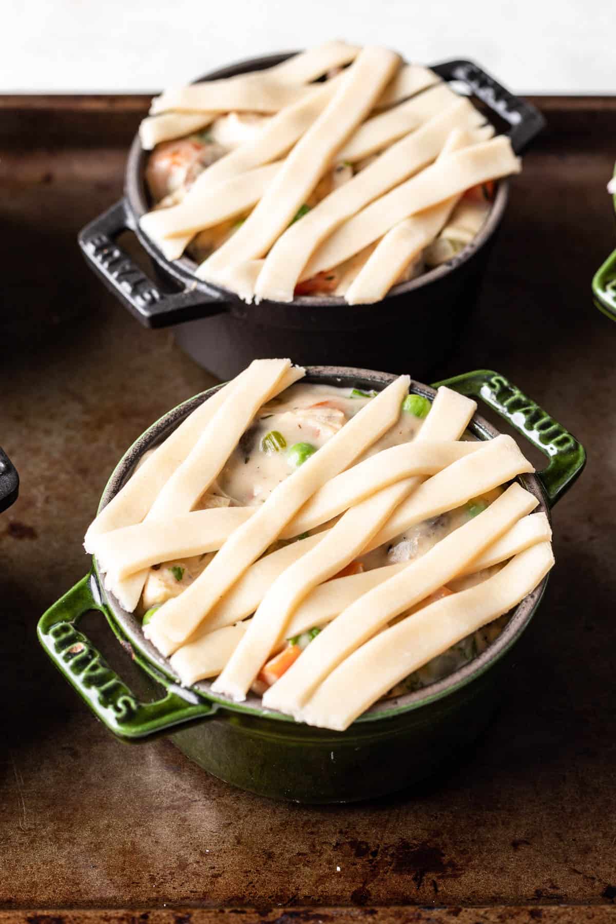 Strips of pie dough forming a lattice crust over chicken pot pie filling in individual cast iron pans.