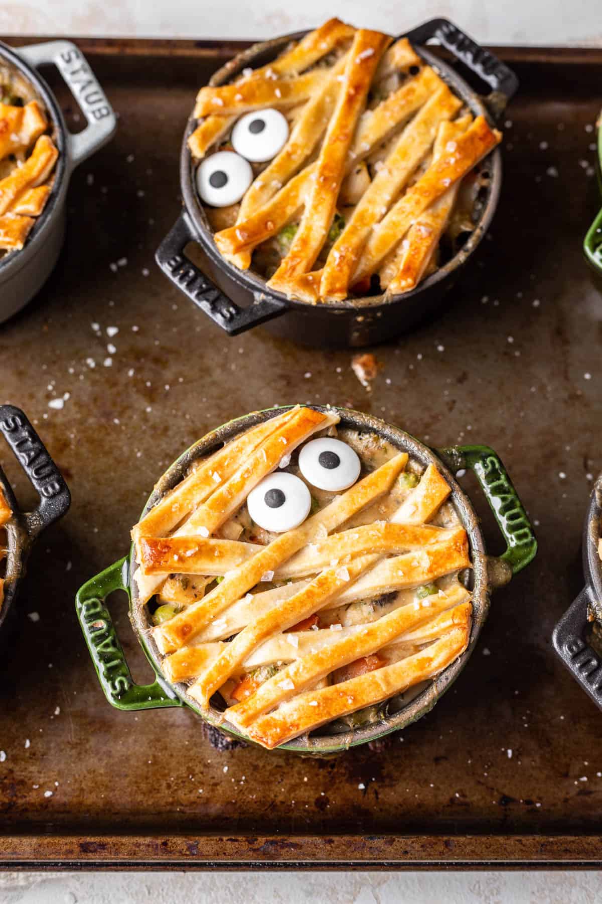 Baked mummy pot pies on a baking sheet decorated with sprinkle candy eyeballs.