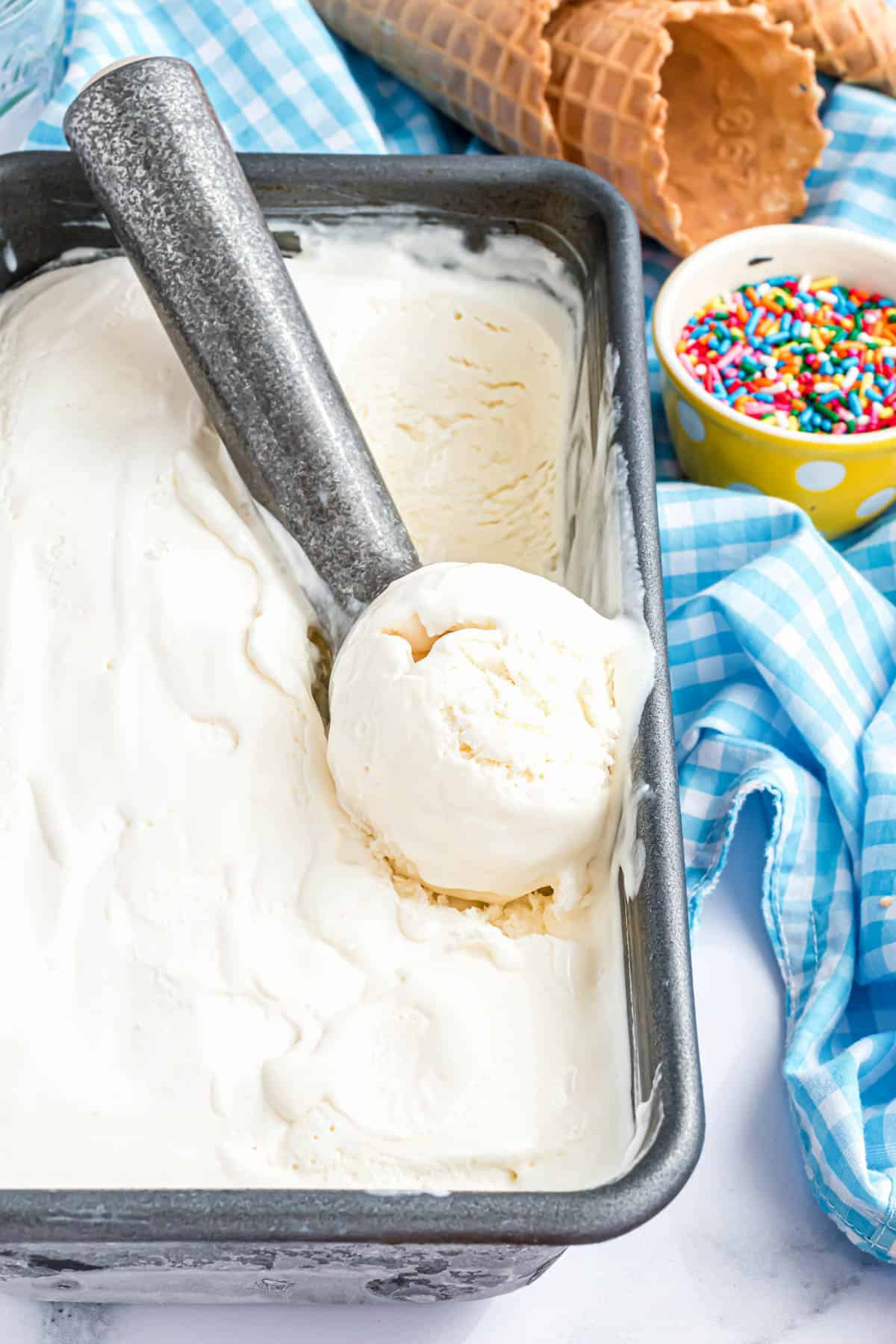 An ice cream scooper in a loaf pan filled with homemade no churn vanilla ice cream.