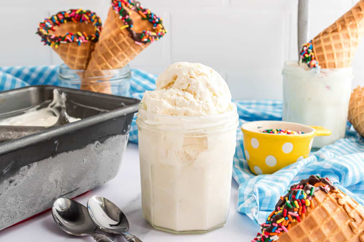 Scoops of no-churn vanilla ice cream in a glass next to a frosty loaf pan filled with more ice cream.