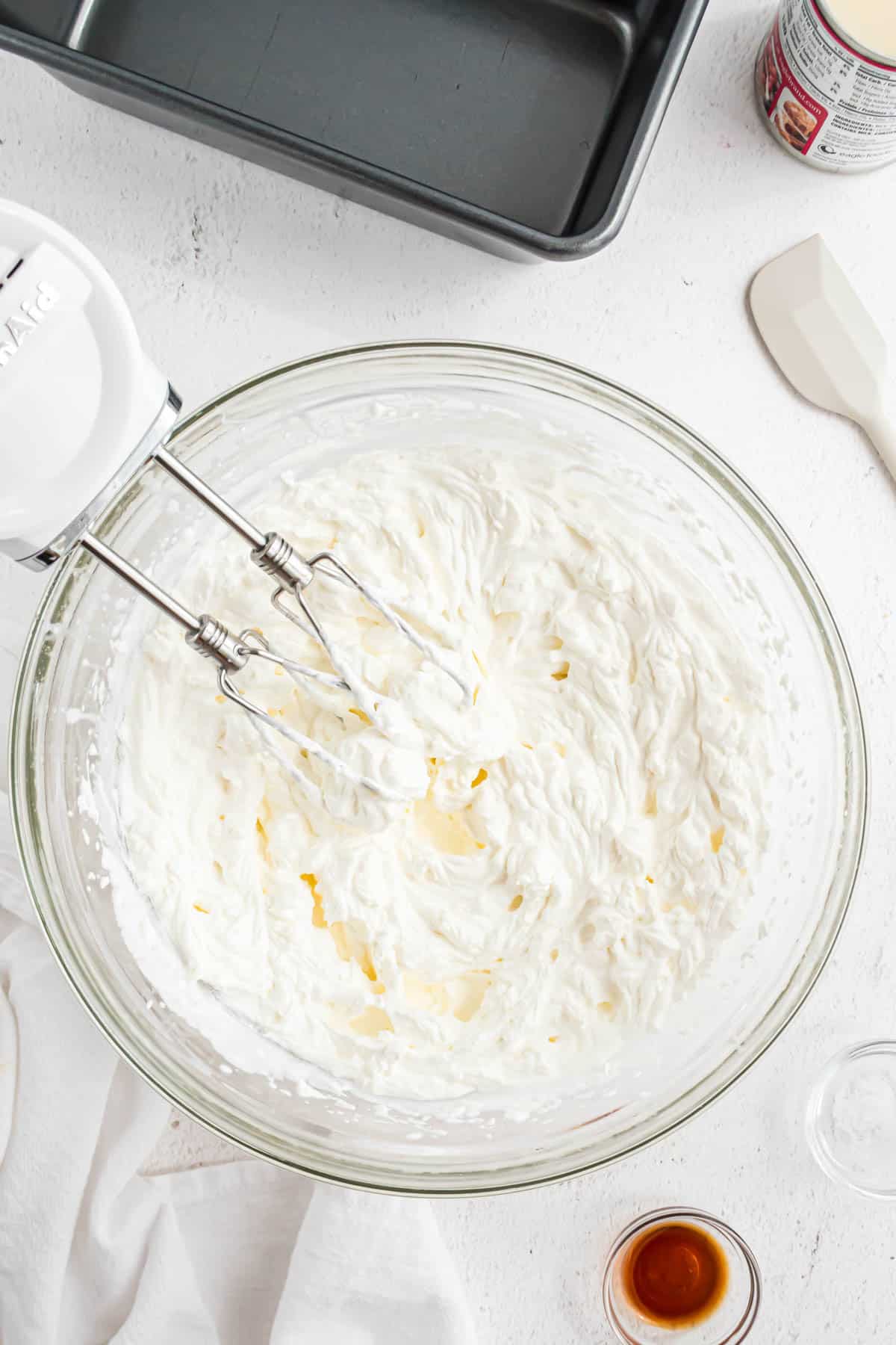 A hand mixer being used to beat heavy cream into stiff peaks in a glass bowl.
