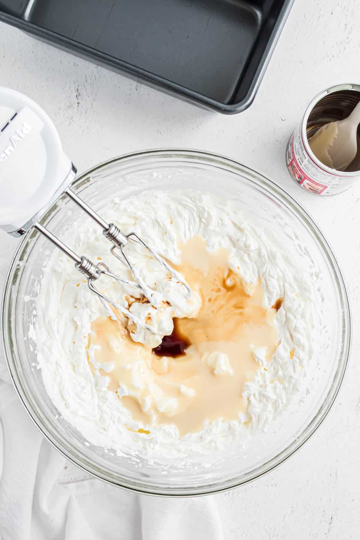 A large bowl with whipped cream, sweetened condensed milk, and vanilla extract.