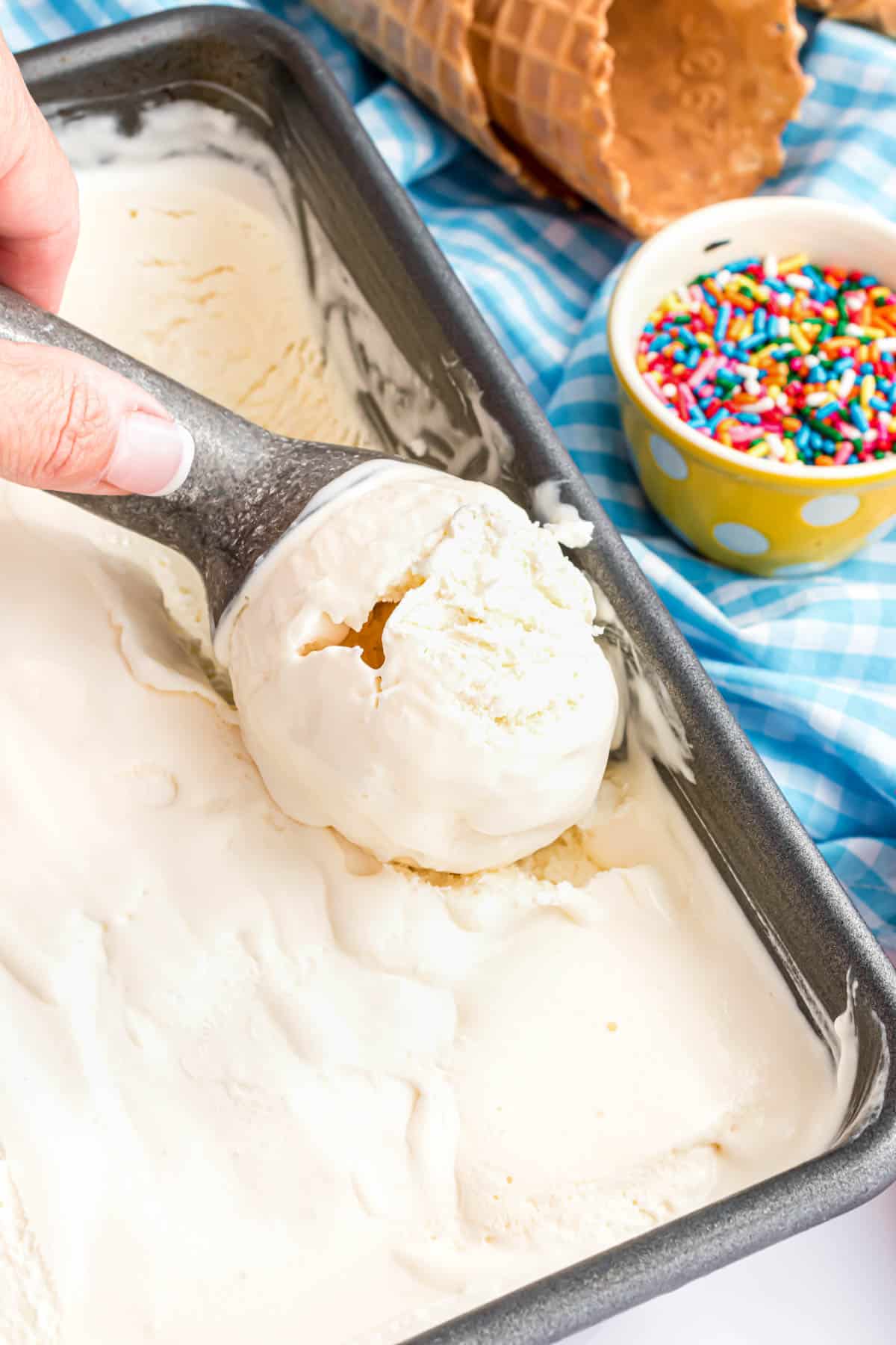 A hand holding an ice cream scooper to scoop vanilla ice cream from a container.