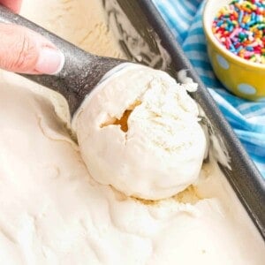A hand scooping homemade no churn vanilla ice cream next to a bowl of sprinkles.