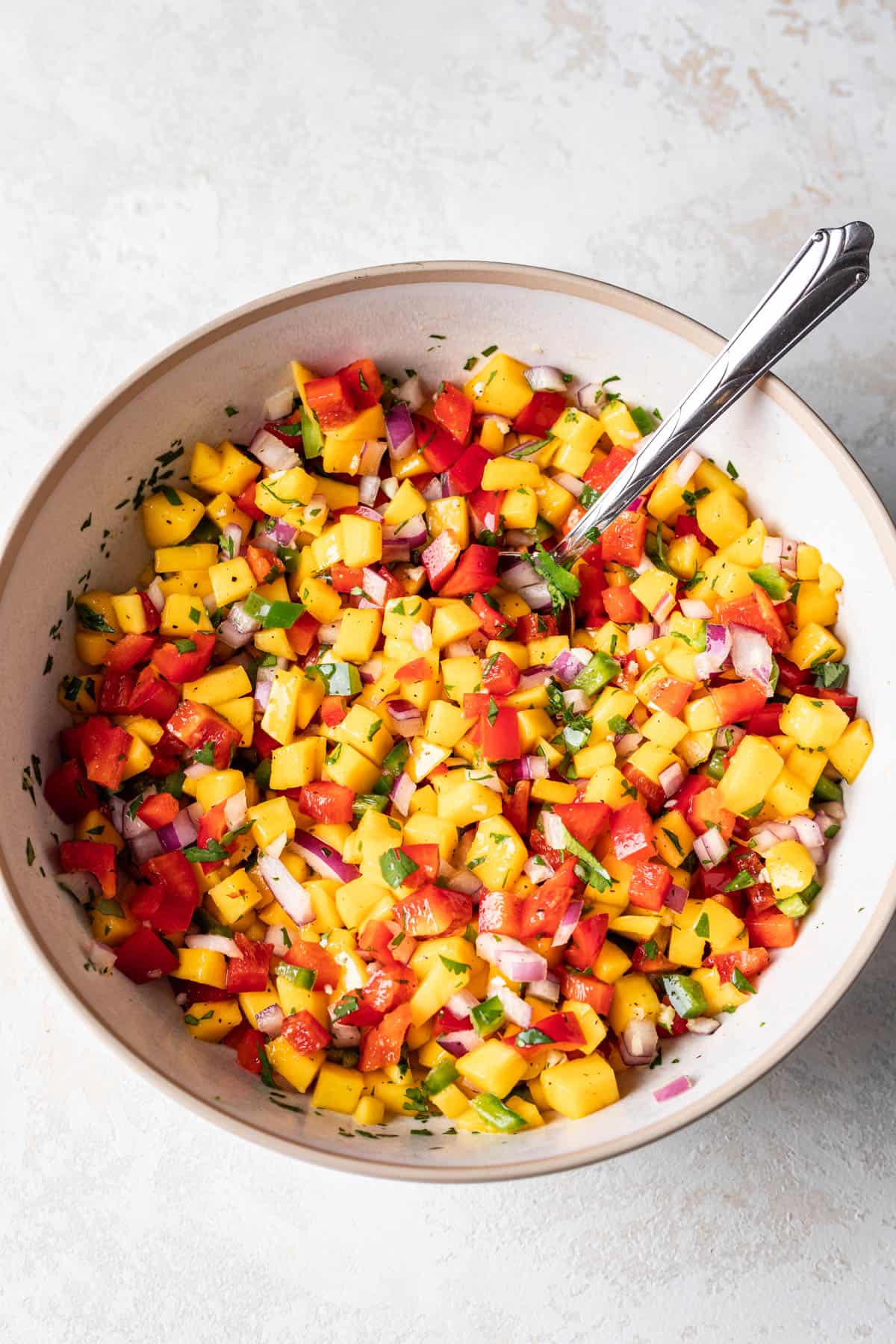 A bowl of fresh mango salsa with a spoon in it.
