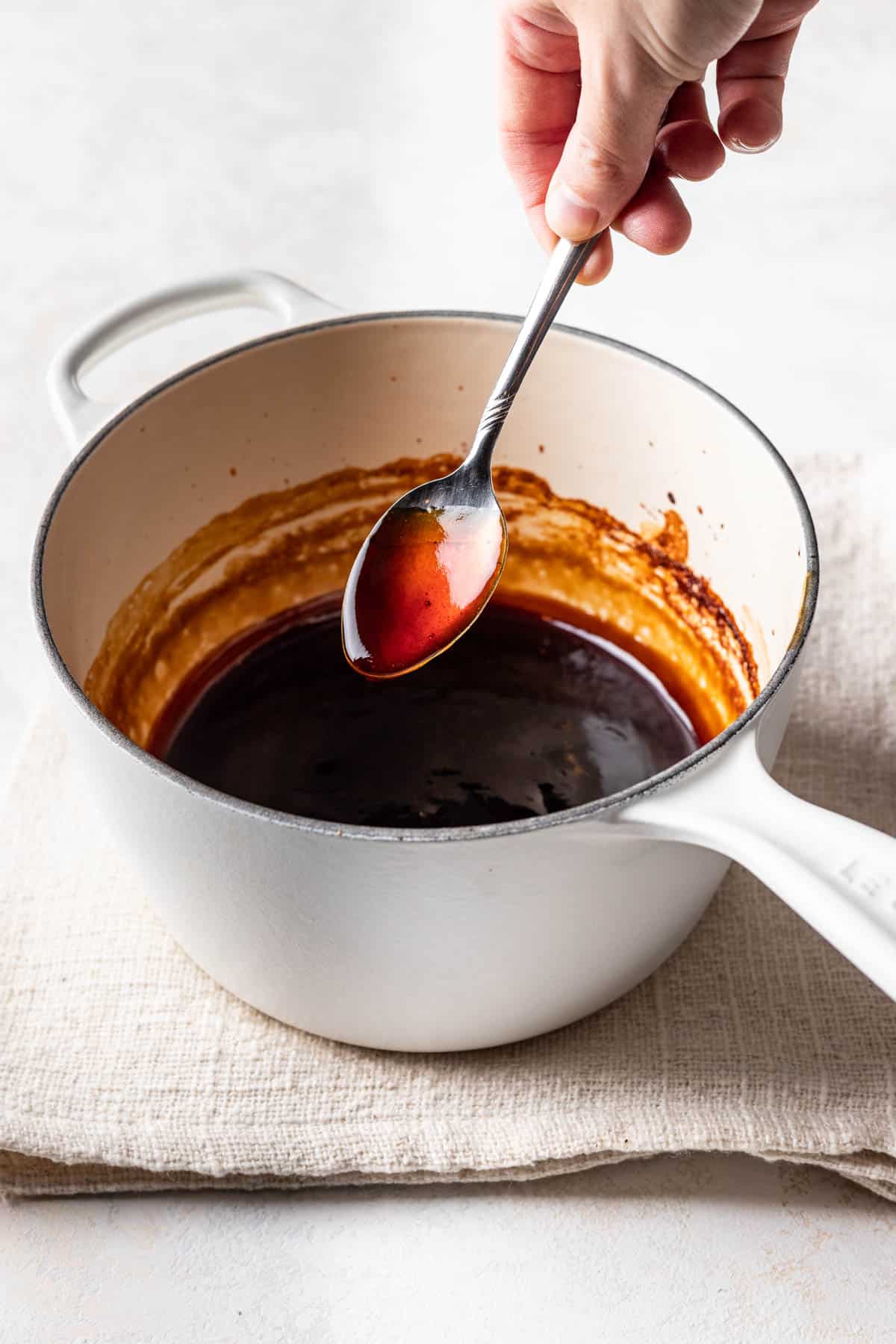 A spoon lifting maple soy glaze out of a saucepan.