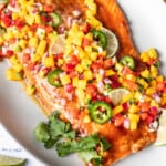 A close-up image of homemade mango salsa and sliced jalapenos topping baked salmon.