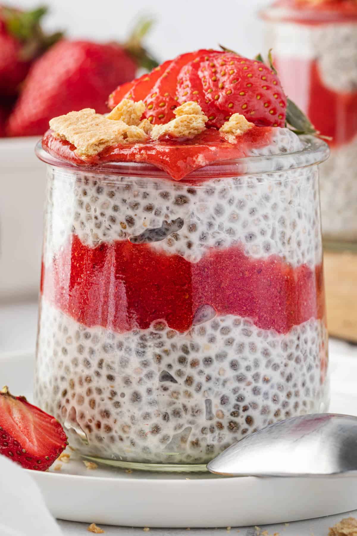 A single serving jar of strawberry cheesecake chia pudding with a sliced strawberry and graham cracker crumbs on top.