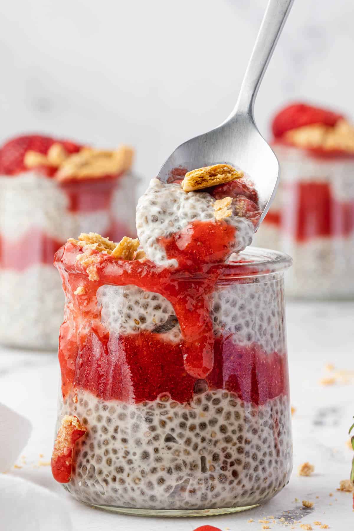 A spoonful of strawberry cheesecake chia pudding lifting next to an individual serving jar.