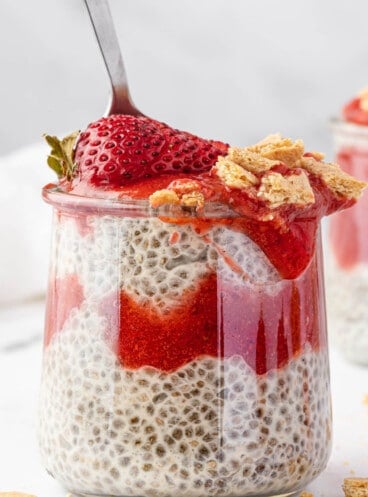 A single serving of strawberry cheesecake chia pudding with a spoon sticking out of it.