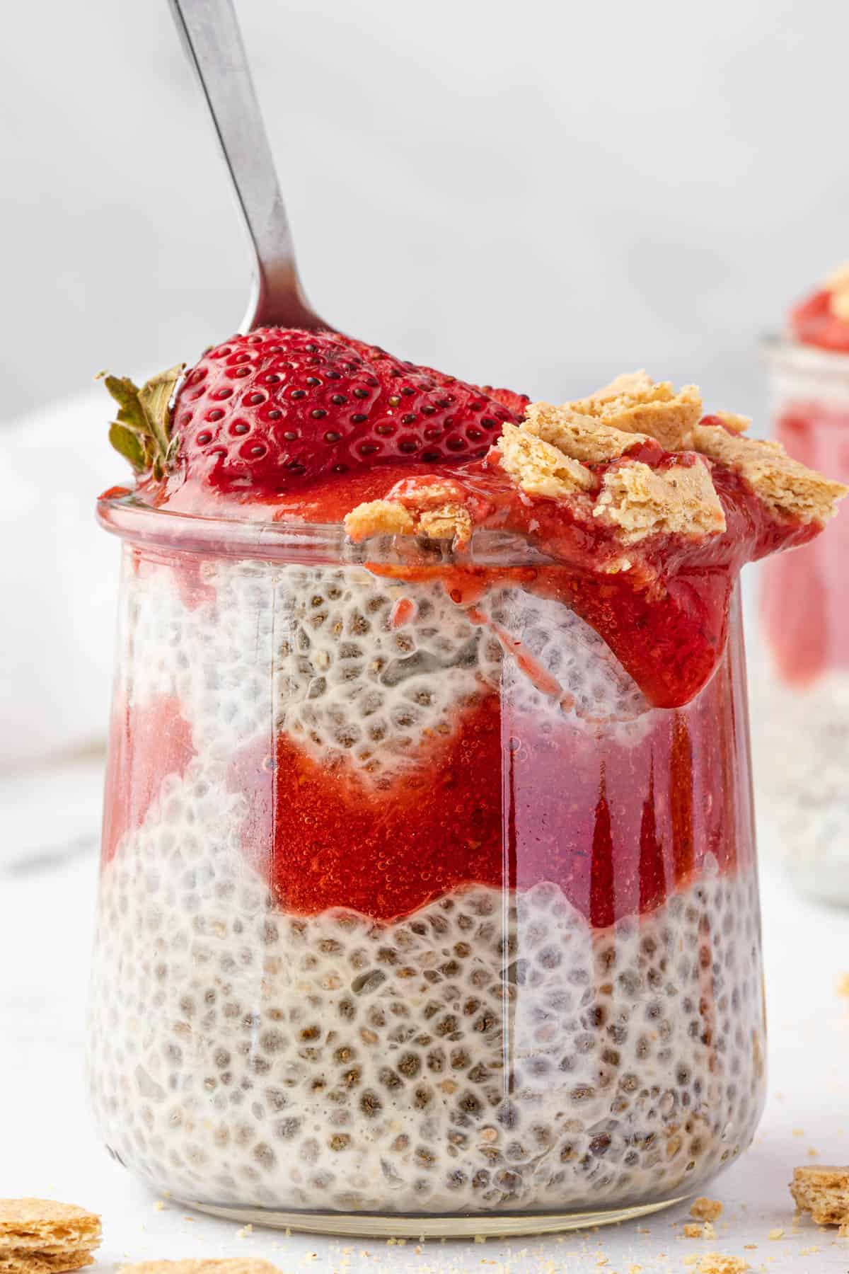 A single serving of strawberry cheesecake chia pudding with a spoon sticking out of it.