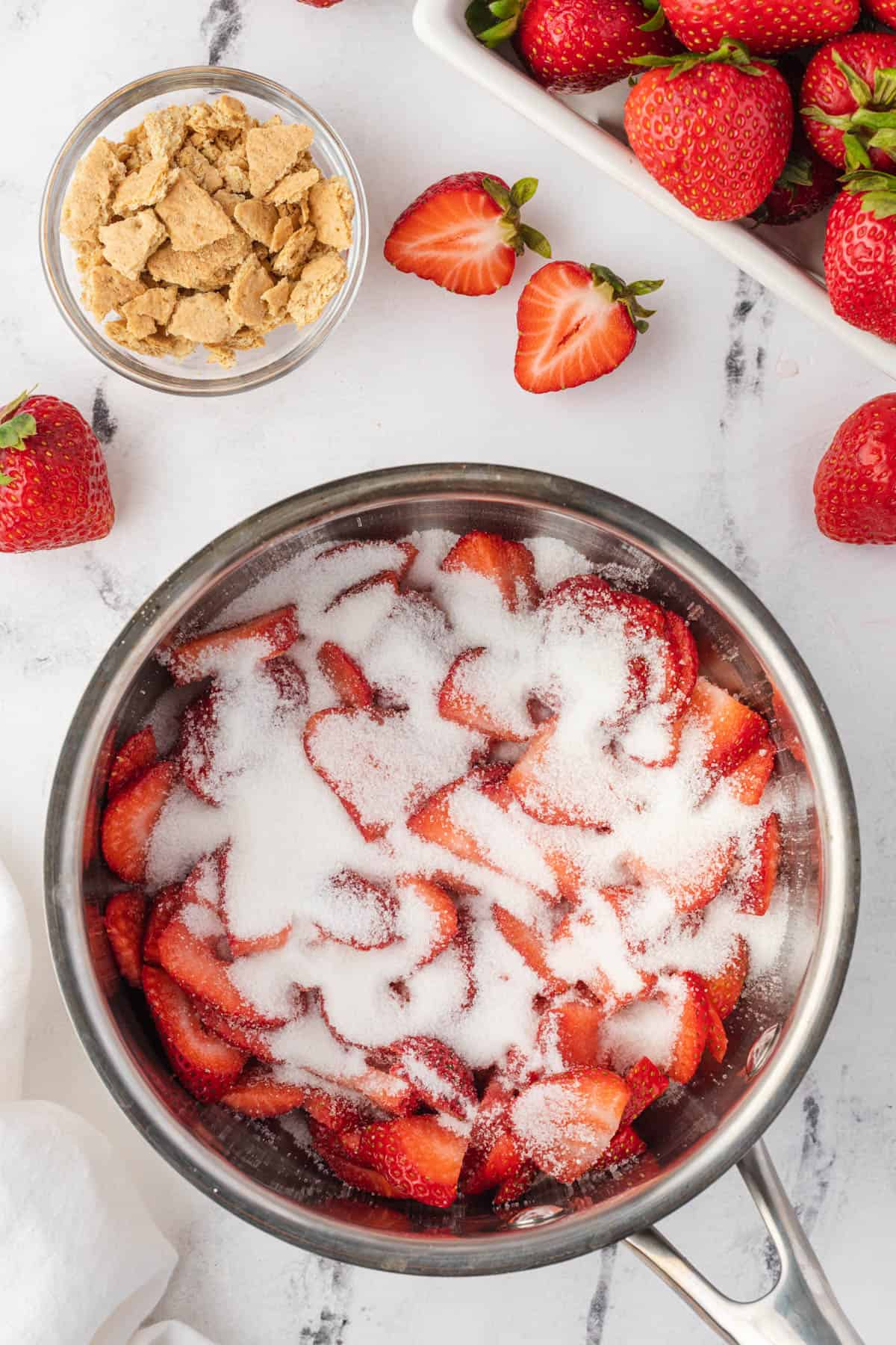 Sugar sprinkled over sliced strawberries in a sauce pan.